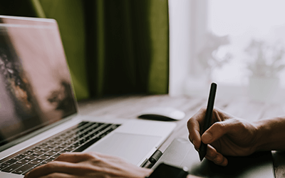 person at laptop writing with paper and pen