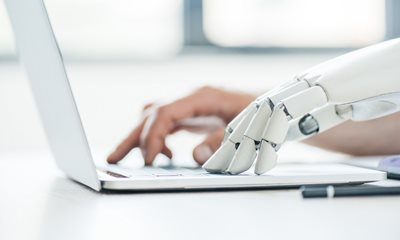 a persons hand and a robot hand typing on a laptop