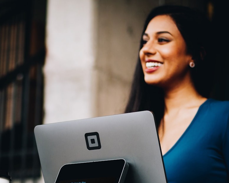 A woman smiles while holding a laptop, conveying a sense of happiness and engagement with technology.