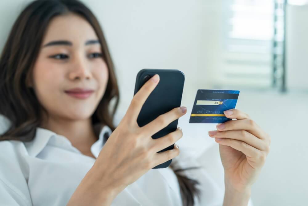 Asian woman engaged in online shopping using her smartphone and credit card.