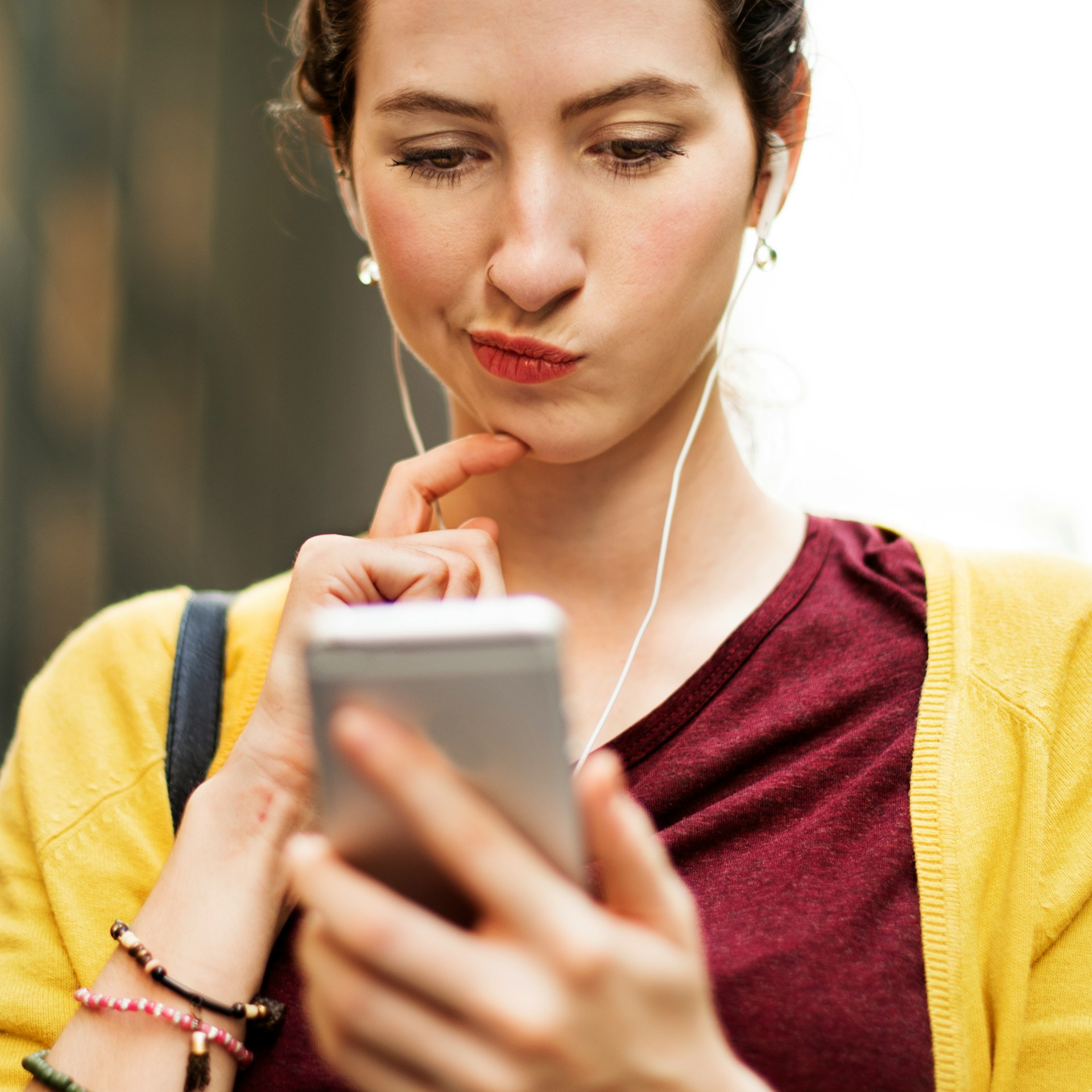 A woman wearing headphones, holding a cell phone, appears focused and engaged in listening or talking.